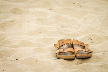 Fototapeta na wymiar A pair of leather sandals in the sand on a beach