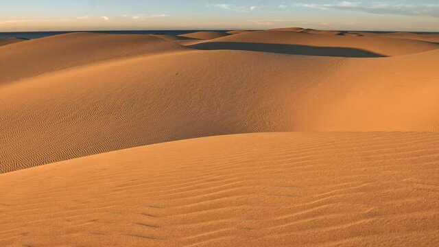Natural Dune Reserve of Maspalomas, Gran Canaria, Spain. Elevating above orange sand dunes in evening. Long shadows. 4K