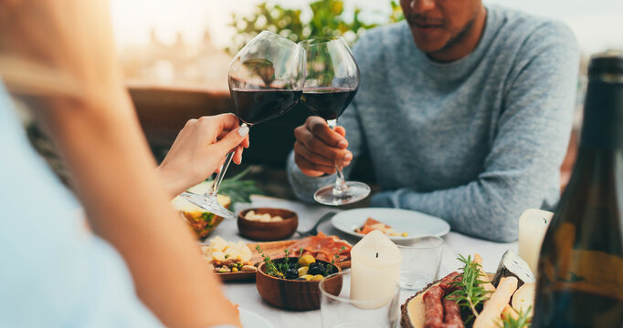 Couple Enjoying Romantic Dinner At Restaurant Terrace Drinking Red Wine And Eating Healthy Mediterranean Food, Lovely Couple Making Cheers With Red Wine Glasses At Summer Day At Terrace