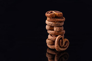 Cookies in the form of a heart with powdered sugar.Delicious, fresh cookies are stacked in a column on a black background. Delicious dessert.