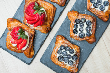 Delicious puff pastries with berries and sugar powder on wooden background
