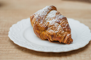 Cold black coffee with ice cubes in tall glass and fresh croissant. Refreshing coffee drink on a table gray background.