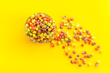 Colorful popcorn in bowl on yellow desk from above