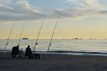 Sports fishermen with fishing rods at the beach of Katwijk aan Zee in the evening at sun set 