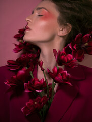 Luxury girl with beautiful pink make-up in a purple jacket and with flowers on a pink background. Good for beauty salons, banners, posters, flyers.
