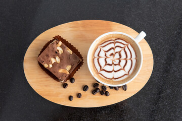 Top view of a white cup of latte art coffee, brownies and coffee beans on wooden plate