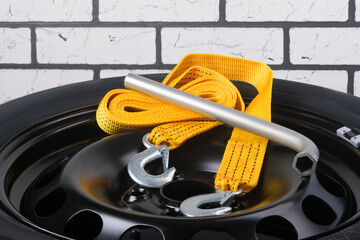 tow rope and wrench lies on a spare wheel, against a brick wall