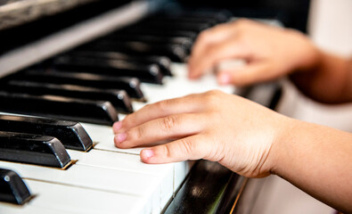 Obraz premium Close up of a little student's hands is playing, learning and practicing the piano. Piano chords In the key of C major. Music abilities for kids. Hobby and activity for the children. Selective focus.