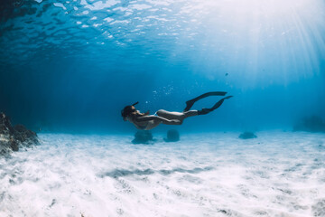 Sporty woman freediver with fins glides over sandy bottom underwater in ocean