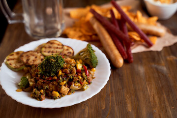 Grilled vegetables with sausage and Mexican corn chips nachos lie on a wooden table.