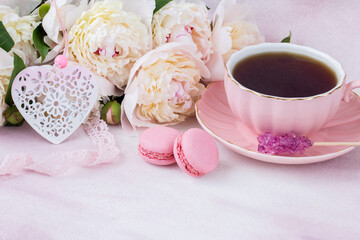 on the table is a cup of tea, sugar, macaroons, heart and pink lace and white peonies 