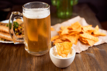 Mexican corn chips nachos lie on a wooden table. With beer