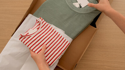 Woman open a box parcel in a box with clothes top view. Concept delivery and online shopping