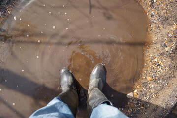 Looking down at welly boots standing in a muddy puddle