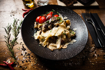 Black Angus pappardelle pasta with beef, champignon and parmegano cheese on a black plate. Delicious healthy mediterranean traditional food closeup served on a table for lunch in modern cuisine