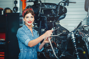 Obraz na płótnie Canvas beautiful girl posing repairs a motorcycle in a workshop, pin-up style, service and sale