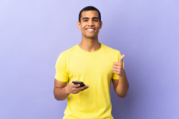 African American man over isolated purple background using mobile phone giving a thumbs up gesture