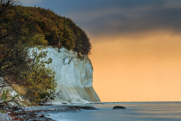 Pirate bay with chalk cliffs in the morning on the island of Ruegen. Coastline for autumn at sunrise. Trees and rocky coastline with leaves and orange clouds in a calm sea
