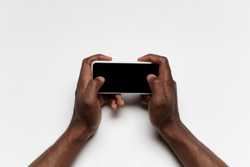Close up of human hands using smartphone isolated on white background. Top view. Copyspace, blank screen. Surfing, online shopping, scrolling, betting, working. Education and business concept.