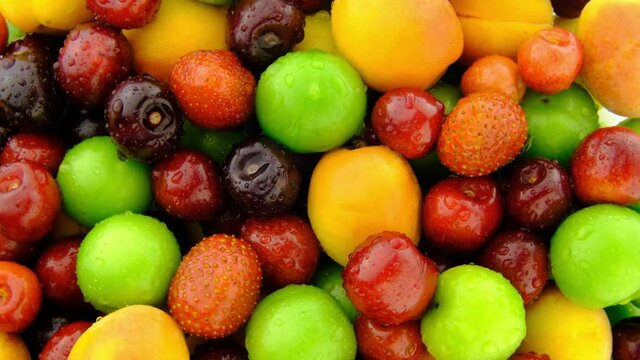 Fruit mix rotating top view background. Fresh organic macro red berry, green plum and yellow apricot fruit turning real shot 4K closeup background video  water drop.