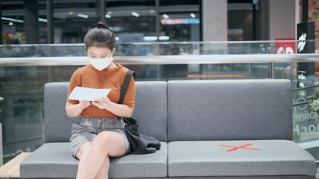 social distancing with asian female wear face mask virus protection waiting sit in chair hand use smartphone communication with space social distance for preventing virus spread