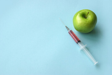 Green apple and syringe with GMO on a blue background.