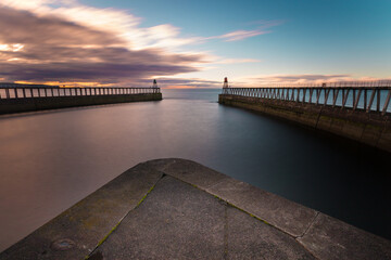 View from Whitby harbour with the piers and lighthouses. Evening sky and calm water