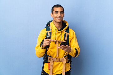 African American man with backpack and trekking poles over isolated background sending a message...
