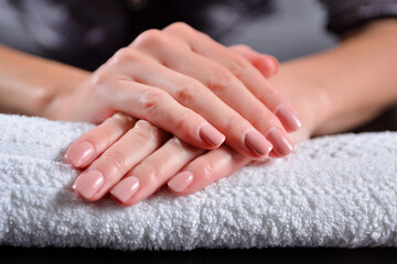 Female hands with nude color nails polish on a towel in beauty studio. Girl holding hand on desk and nails colored with natural nude shade color. Manicure concept. Close up, selective focus