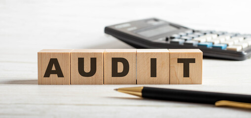 The word AUDIT is written on wooden cubes between a pen and a calculator. Business concept