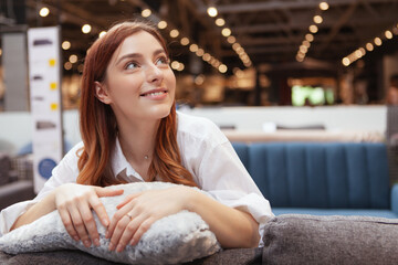 Lovely young woman smiling, looking away dreamily while shopping for new furniture at home goods...