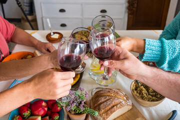 Four people friends or family toasting with red wine glasses having fun together around the table with vegetarian food. Healthy eating and relax concept