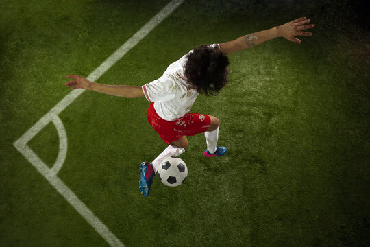 Top view of caucasian football or soccer player on green background of grass. Young male sportive model training in action. Kicking ball, attacking, catching. Concept of sport, competition, winning.