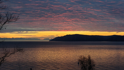 Beautiful Lake Landscape at Sunset Sky Sun over the Mountains on Lake Baikal, Siberia. Magnificent Sky with textured Clouds. Twilight time. Popular Travel Destination. Panorama