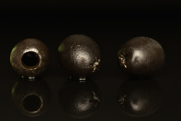Pickled spicy black olives, close-up, on a black background.