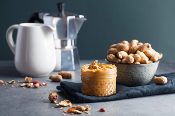Closeup peanut butter in a glass jar, a handful of peanuts in shell. Foodphoto. Copy space. Breakfast for vegetarians. 