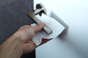 Close up of hand cleaning and disinfecting door handle surface with antiseptic