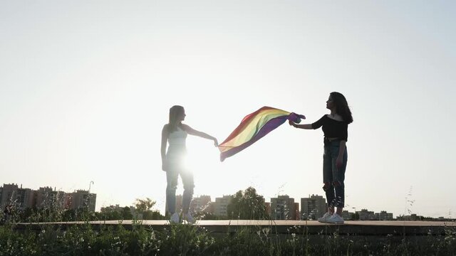 two young girls with the LGBT gay pride flag flying in the wind at sunset