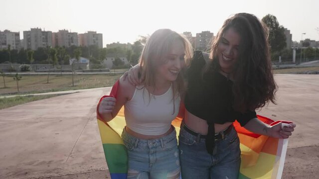 two young girls walking and laughing with the LGBT flag of gay pride at sunset