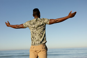 An African American man with his arms outstretched on beach on a sunny day