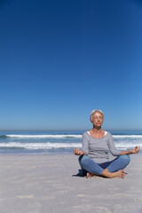 Naklejka na ściany i meble Senior Caucasian woman meditating at the beach.