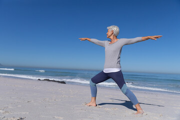 Senior Caucasian woman practicing yoga at the beach.