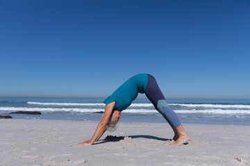 Senior Caucasian woman practicing yoga at the beach.