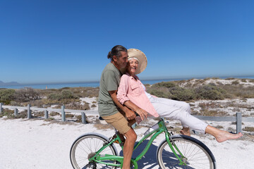 Fototapeta premium Senior Caucasian couple riding a bike at the beach