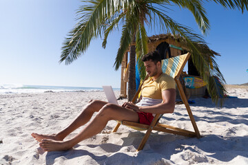 Caucasian man  sitting on a deck chair and using a laptop at the beach