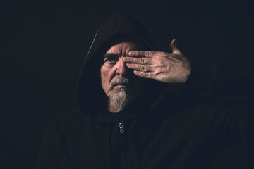 portrait of a man wearing a hoodie, holding one hand in front of an eye