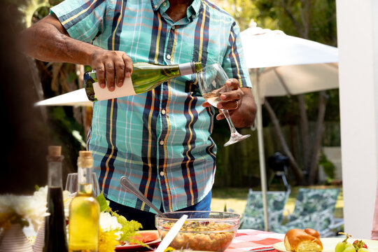 Mid section of a Senior African American man pouring wine into a glass in the garden 