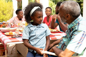 African American girl sitting on her grandfather knees during a family lunch in the garden