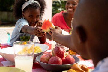 African American girl playing with slices of watermelon during a family lunch in the garden 