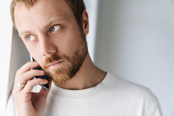 Photo of serious man talking on mobile phone while leaning on wall